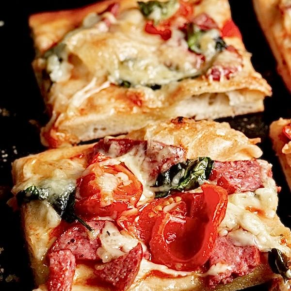 Close-up of a pepperoni and tomato Roman pizza slab