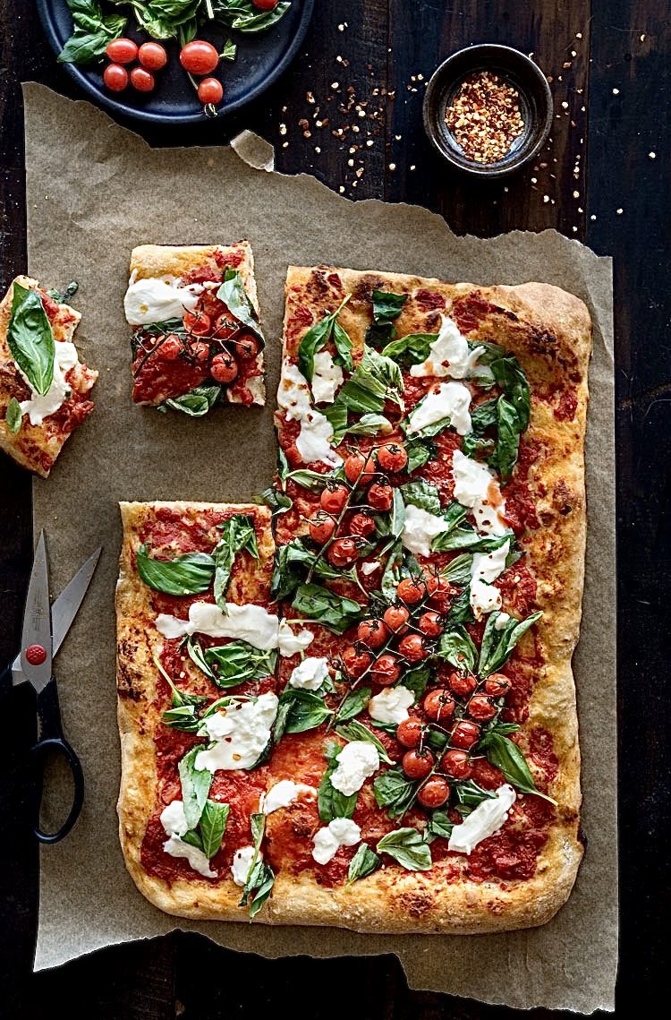 A whole Roman tray pizza with tomato, basil and mozzarella, cut into rectangular slabs on parchment